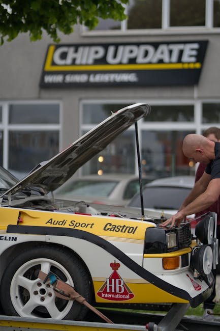 Mechanic inspecting an Audi racing car engine in an outdoor setting with visible company branding.