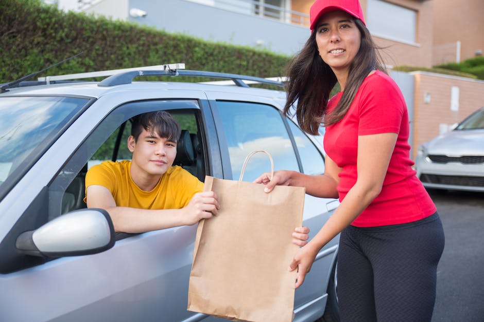 Man in car receiving takeout from woman at drive-through location.