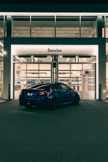 A sleek blue car approaches a well-lit service center entrance at night.